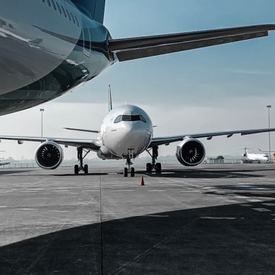 Low angle of various airplanes parked on airfield against blue sky on sunny day